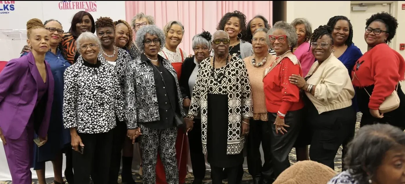 More than twenty women in their brunch best pose together in front of the Real Girlfriends backdrop