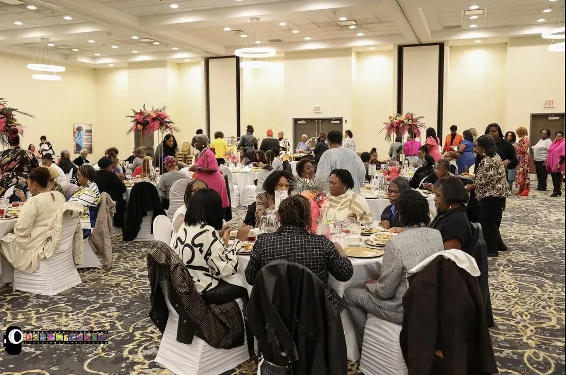 Guests fill long rows of tables decorated with pink floral centerpieces