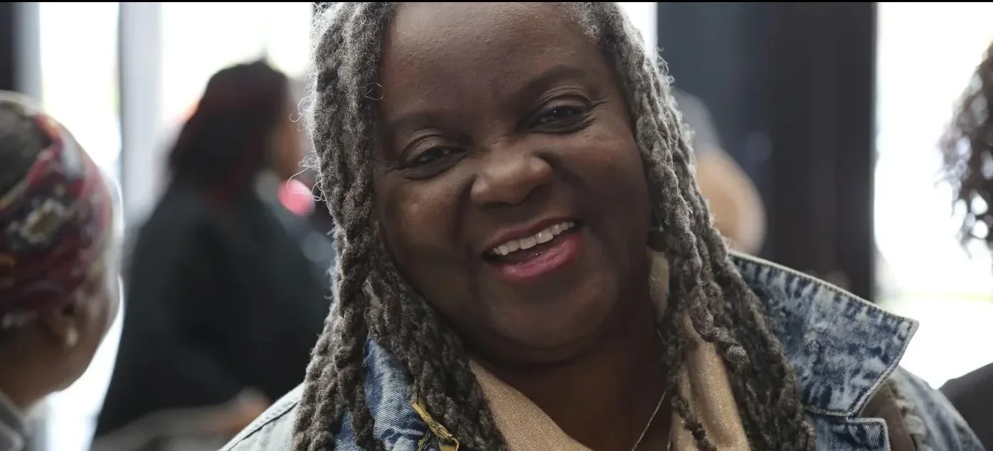 A woman with silver locs beams at the camera