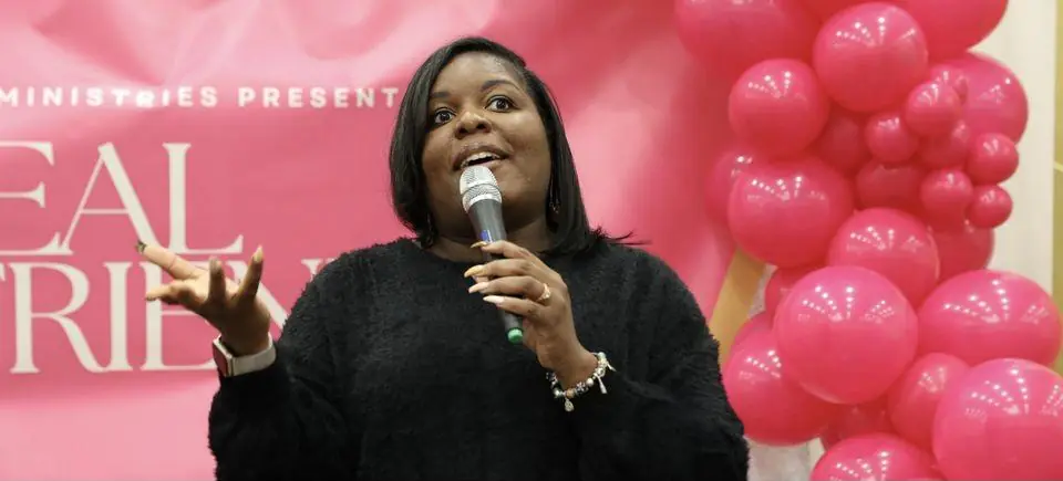 A speaker preaches into the microphone in front of the pink Real Girlfriends backdrop